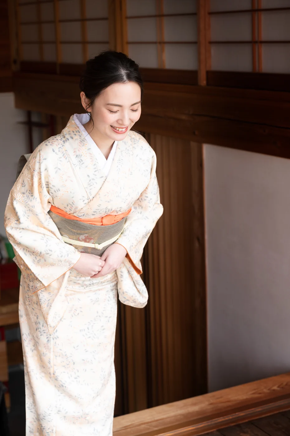 Seorang wanita berkimono warna pucat membungkuk di pintu masuk interior tradisional Jepang.