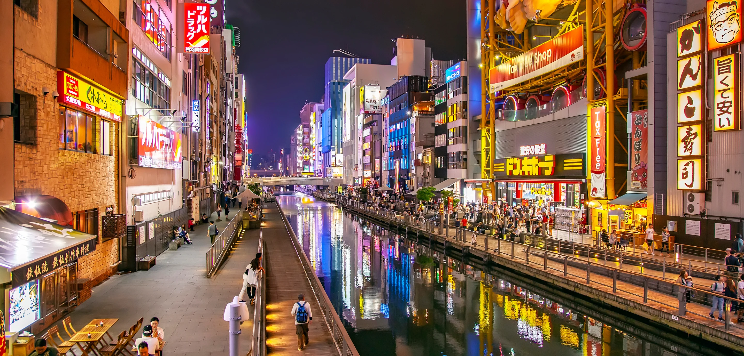 Papan restoran dan cahaya yang terpantul di kanal Dotonbori pada malam hari di Osaka