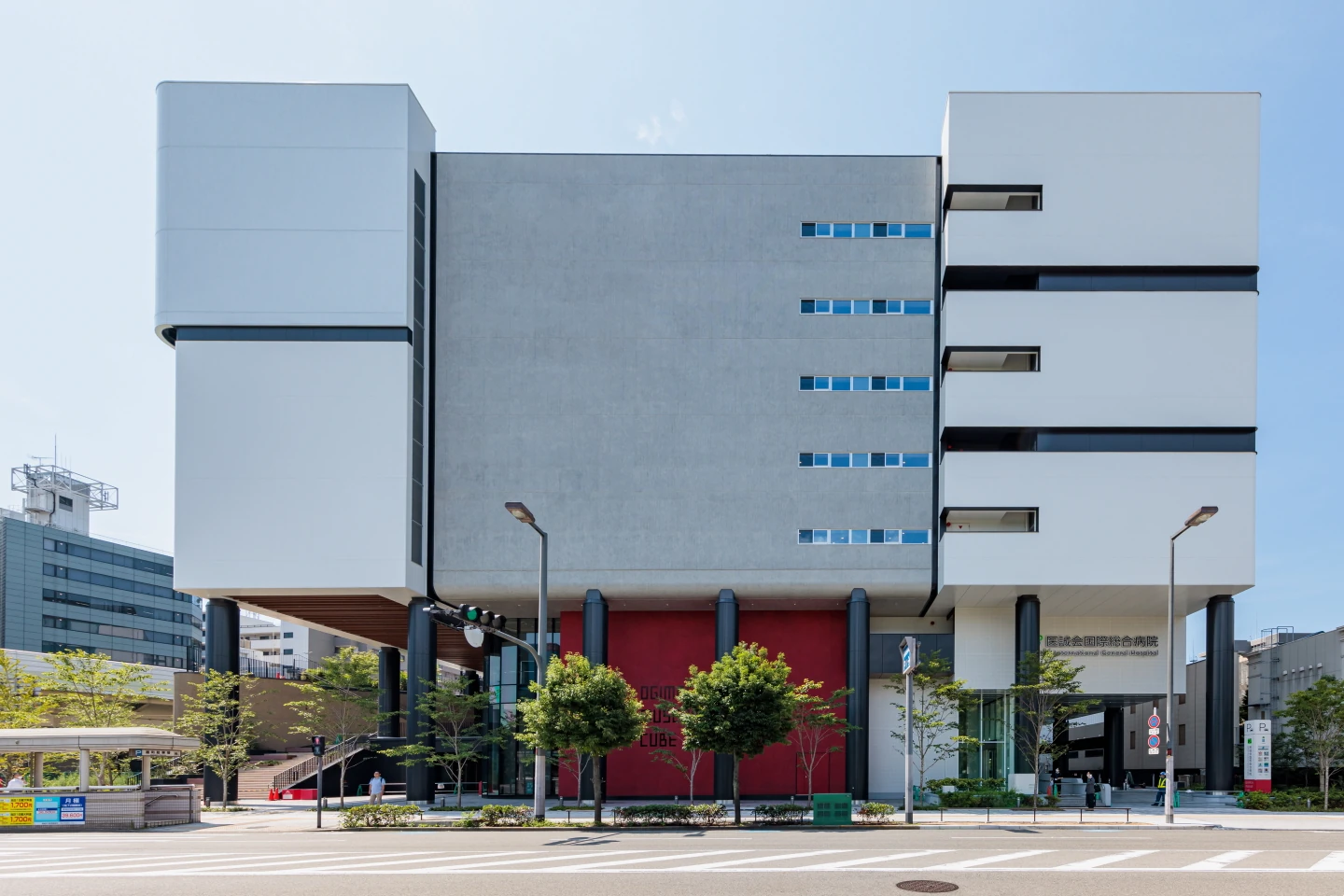 Eksterior gedung rumah sakit putih modern dari jalan, dengan pepohonan di pintu masuk.