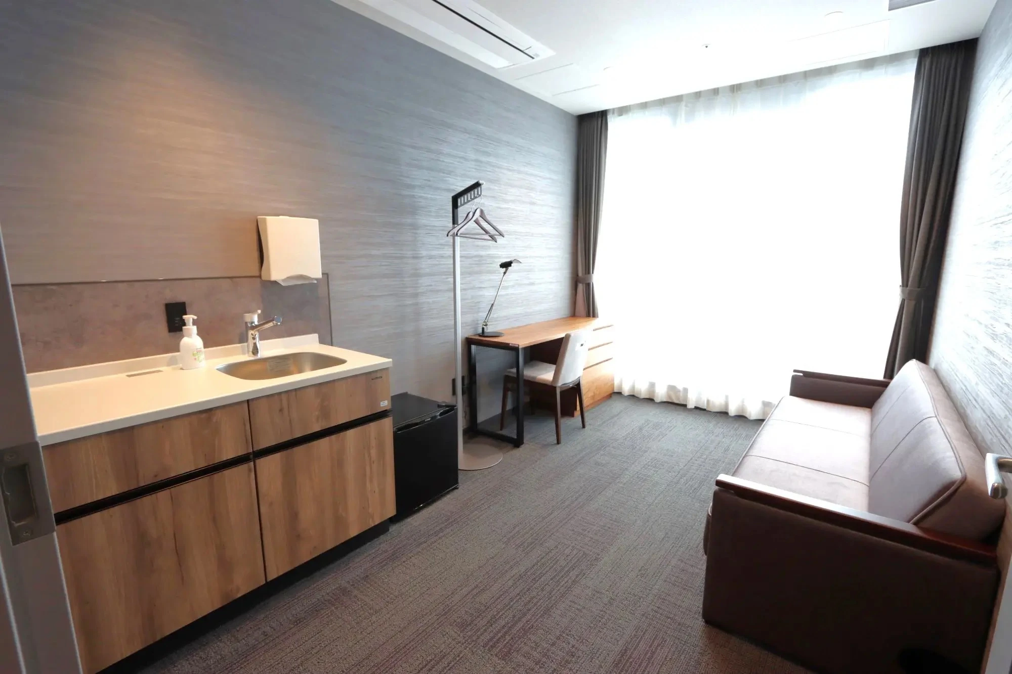 Kamar suite dengan sofa, meja kerja, wastafel, dan jendela besar bertirai.