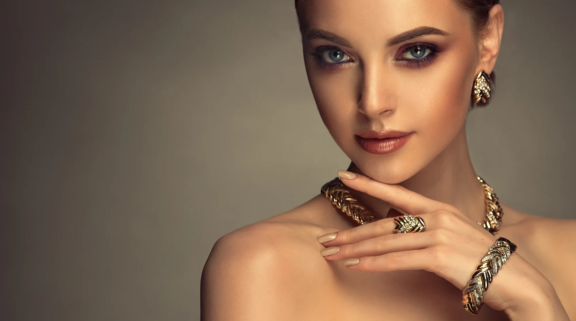 Potret perempuan mengenakan anting, cincin, dan gelang emas, dengan tangan di dekat wajah.