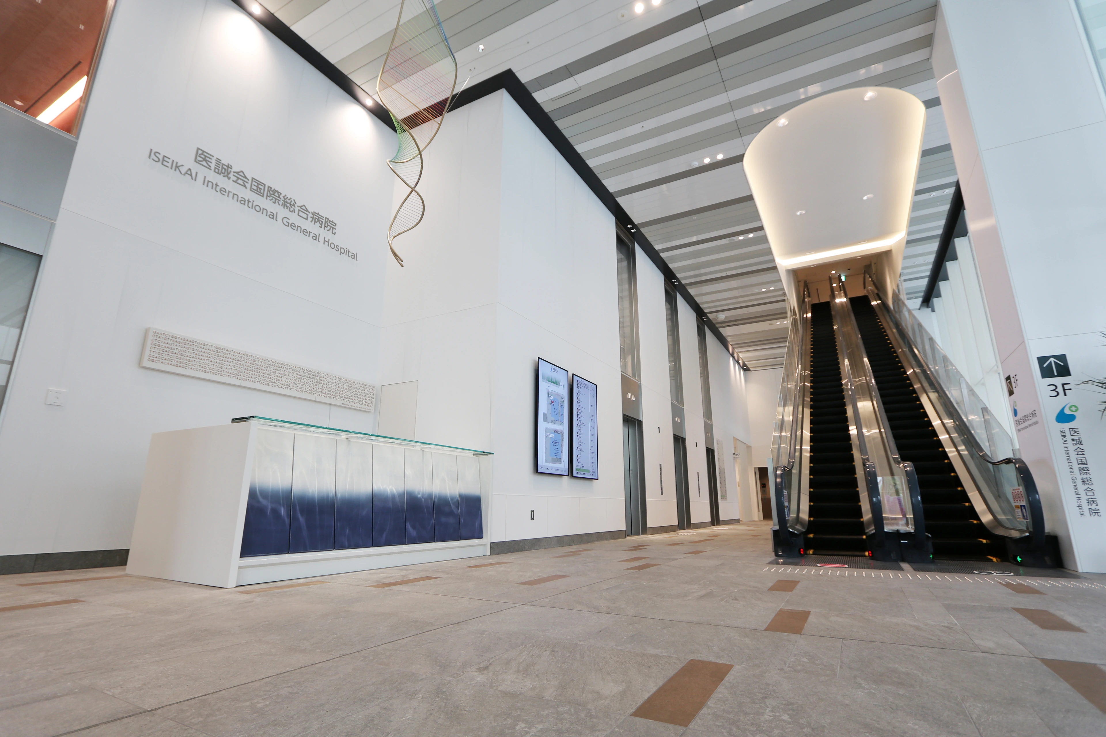 Lobi pintu masuk menara utara Iseikai International General Hospital, dengan atrium dan eskalator.