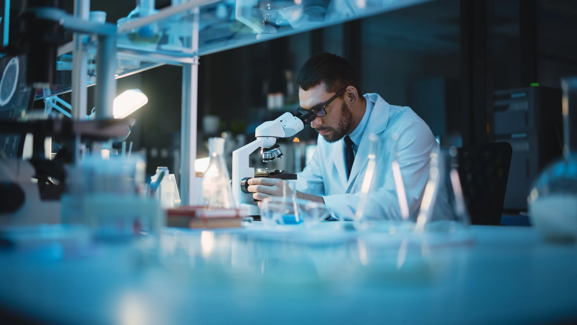 Peneliti menggunakan mikroskop di laboratorium dengan pencahayaan biru.